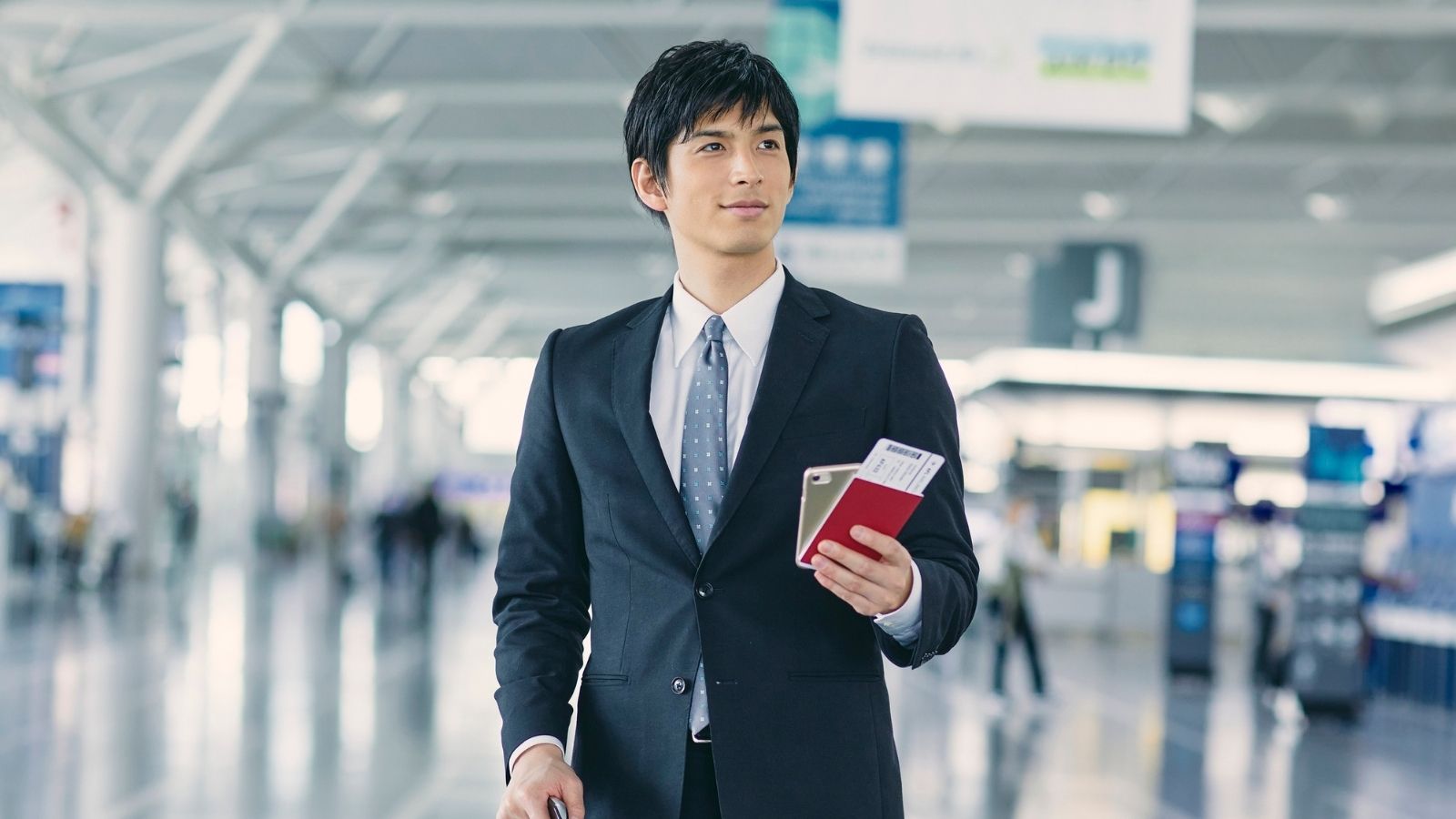 A traveller in business dress holding a passport and boarding pass in an airport terminal — tax residency planning with Global Investments for people who live and work across borders