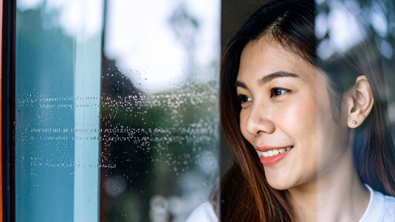 A woman smiling as she looks out through a rain-speckled window — the virtual GP and second medical opinion services included in most cover