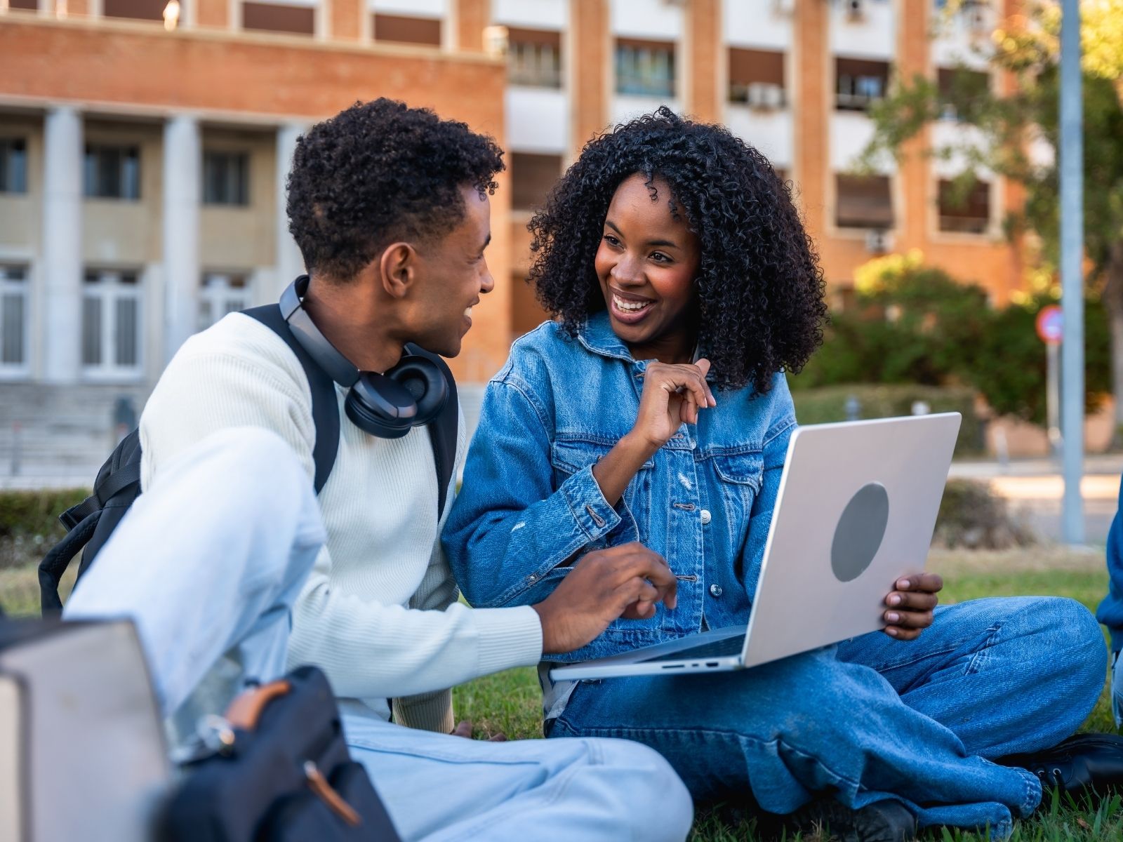 Two students sitting on a campus lawn with a laptop and backpacks — the international schools and education funding hub at Global Investments