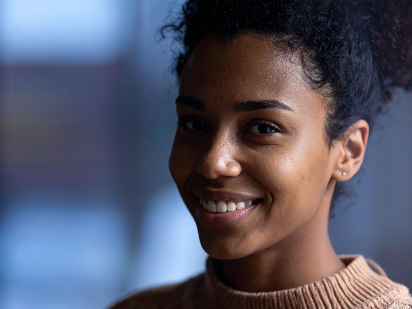 A woman photographed close in warm indoor light, smiling past the camera — direct billing versus paying the hospital first under medical cover